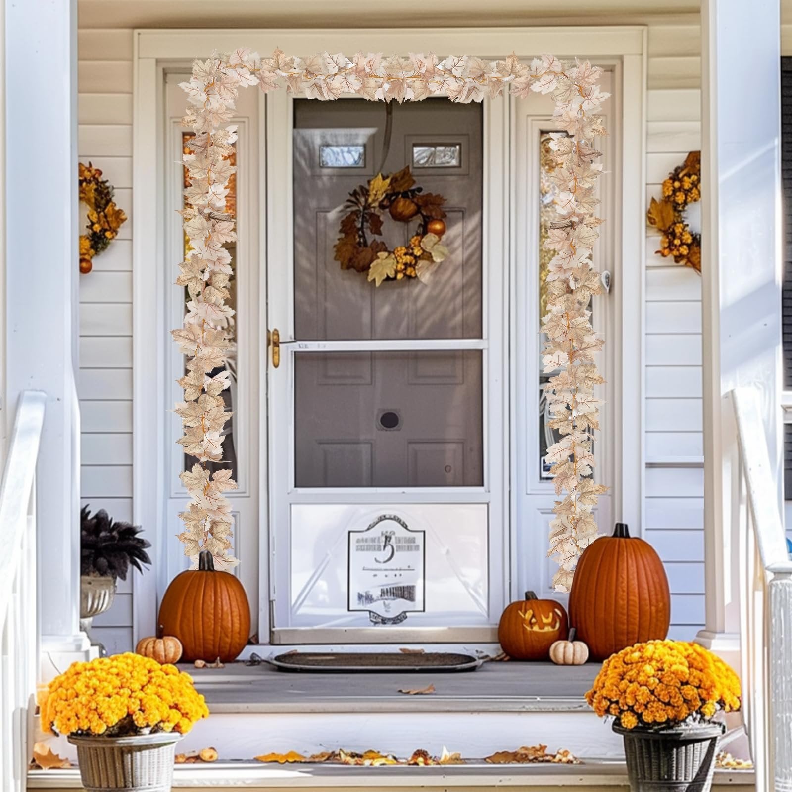 Fall maple leaf garland with lights draped around a front door with pumpkins and mums