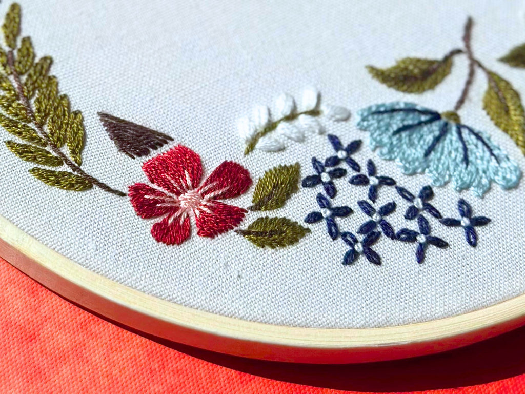 Close-up of an 8-inch floral embroidery kit with a bamboo hoop, featuring red, blue, and white flowers and green leaves stitched on white fabric.