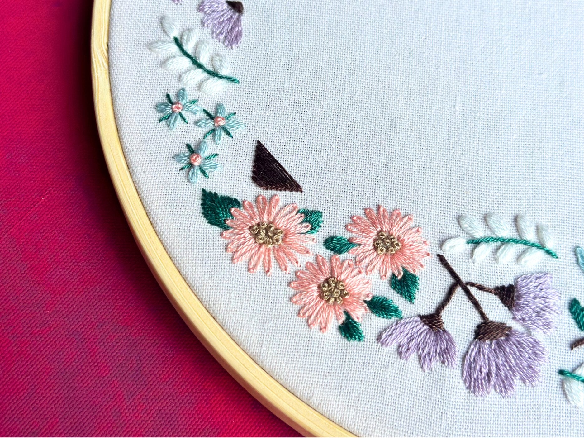 Close-up of a floral embroidery kit with pink, purple, and blue flowers on white fabric within a bamboo hoop.
