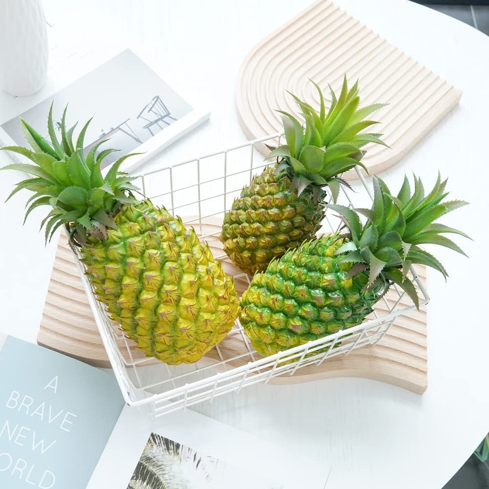 Three artificial green pineapples in a white wire basket on a wooden board.