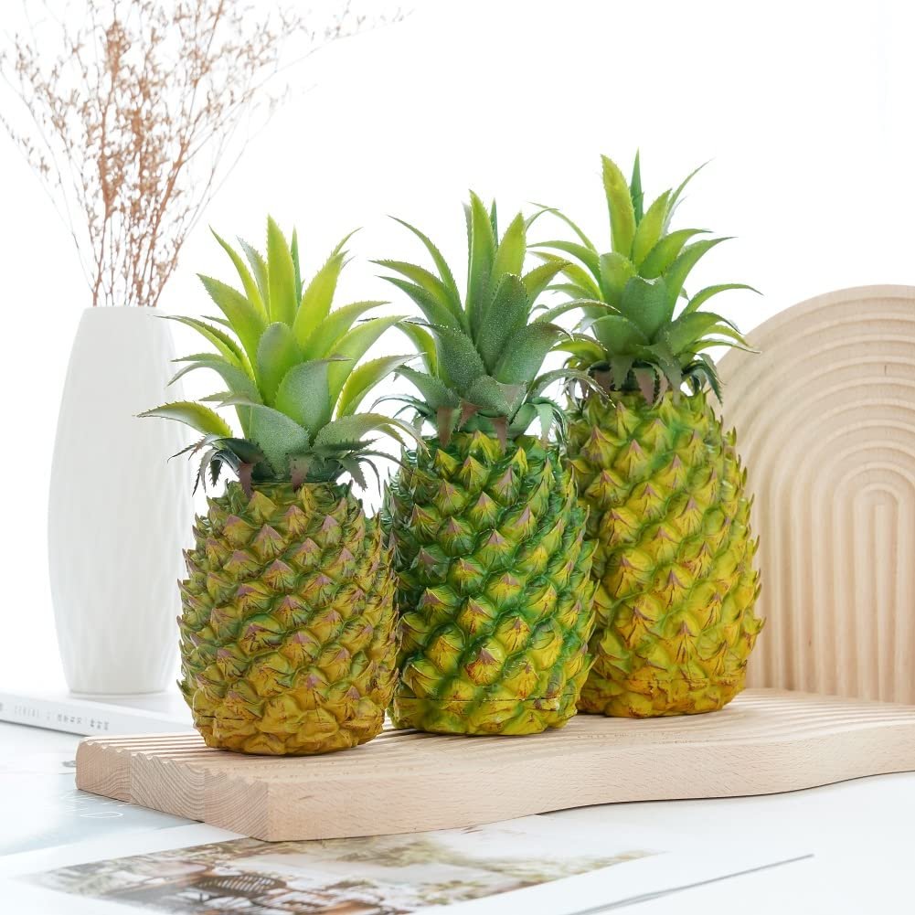 Three artificial pineapples with green tops and yellow-green textured bodies arranged on a wooden shelf.