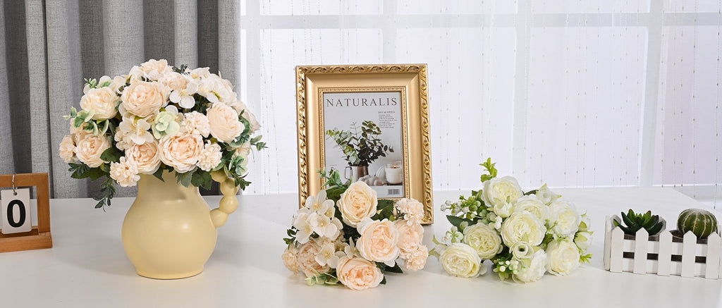 Three bouquets of artificial peonies and roses arranged with a vase and decorative frame