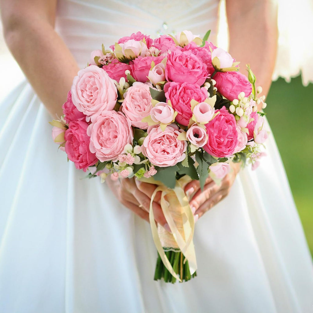 Bride holding a bouquet of pink silk peonies with buds and ribbon.