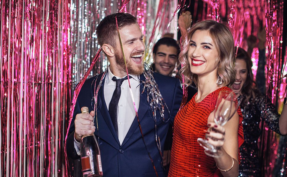 Couple celebrating at a party with pink tinsel fringe backdrop and champagne