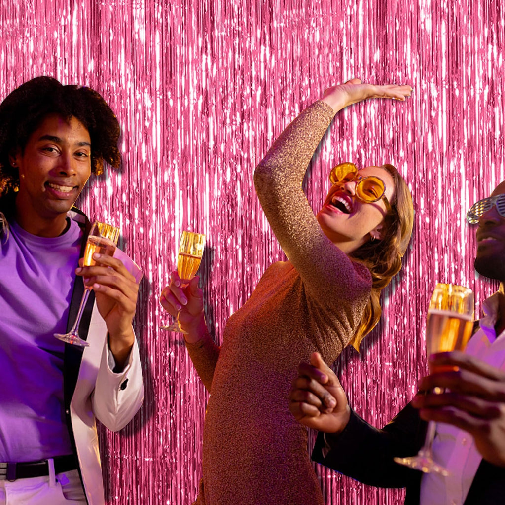 Three people celebrating with champagne in front of a pink tinsel fringe backdrop