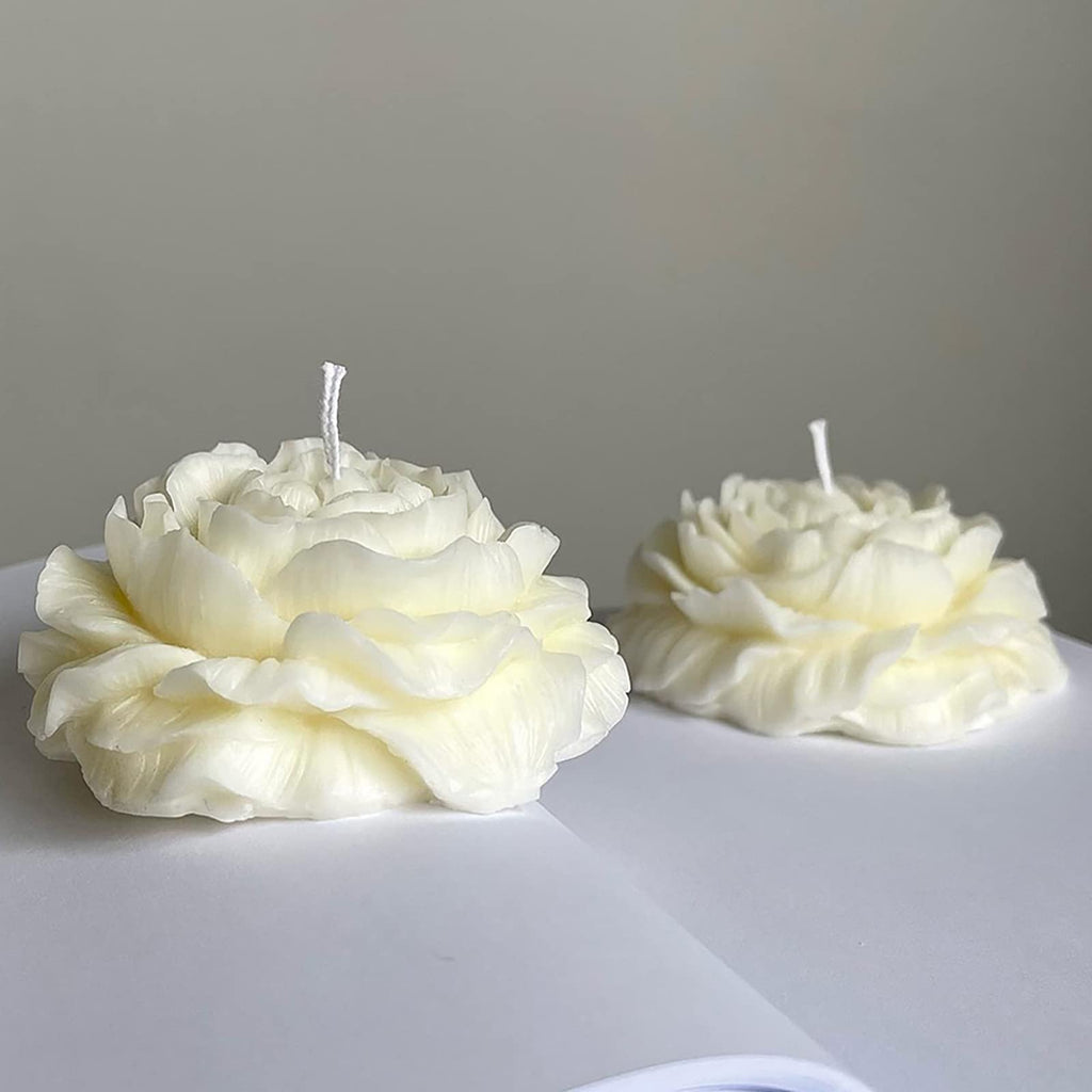 Two white peony-shaped candles with wicks on a white surface against a grey background.