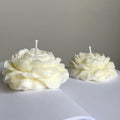 Two white peony-shaped candles with wicks on a white surface against a grey background.