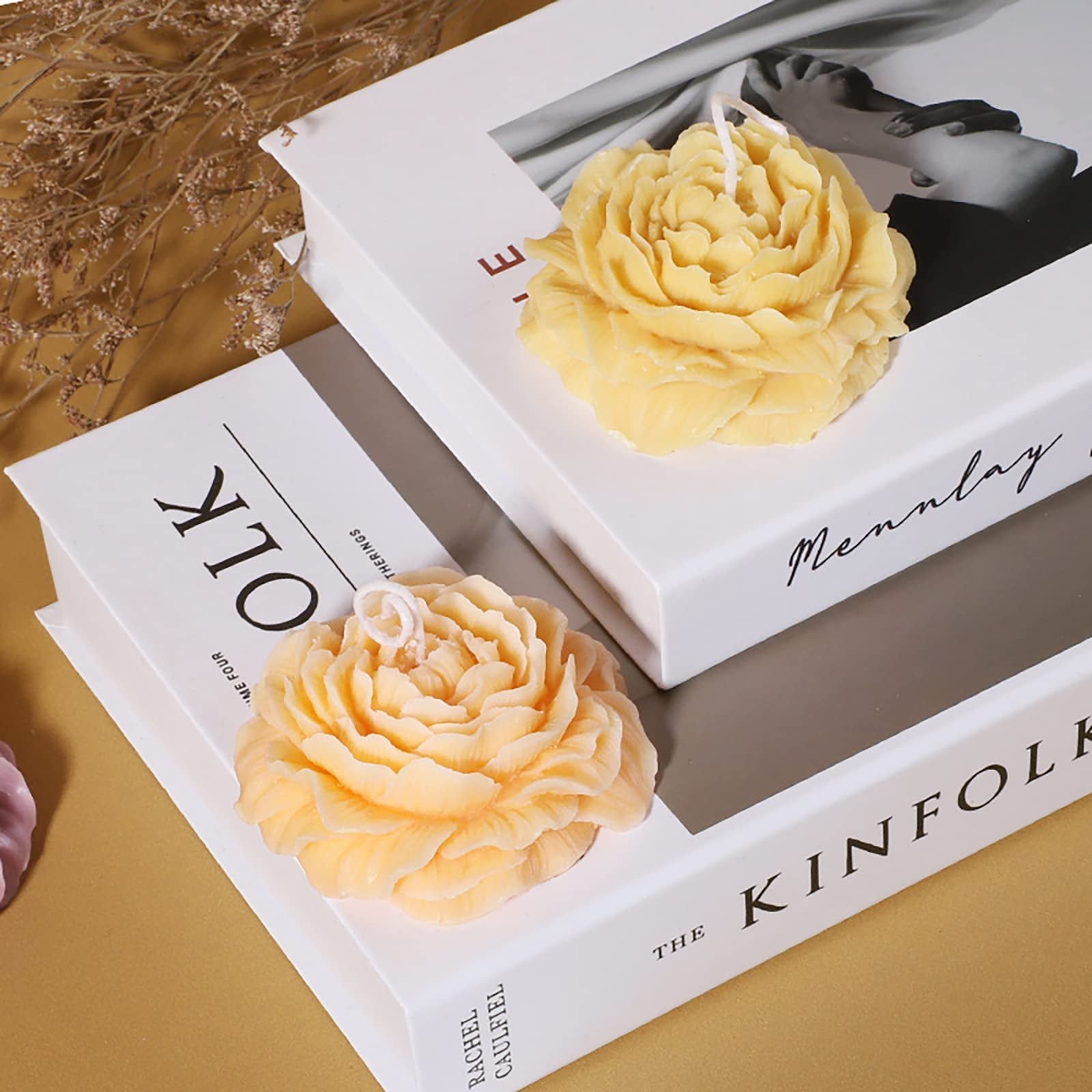 Two floral-shaped candles, one yellow and one peach, resting on decorative books.
