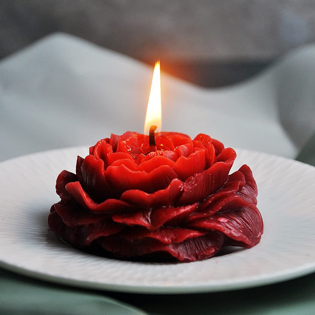 Red peony-shaped candle with a lit wick, resting on a white plate.