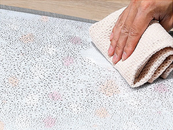 Close-up of a hand wiping a textured surface with a waffle-weave cloth, showing small droplets.