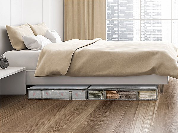 Two under-bed storage containers filled with folded linens, placed on a wooden floor beneath a bed.