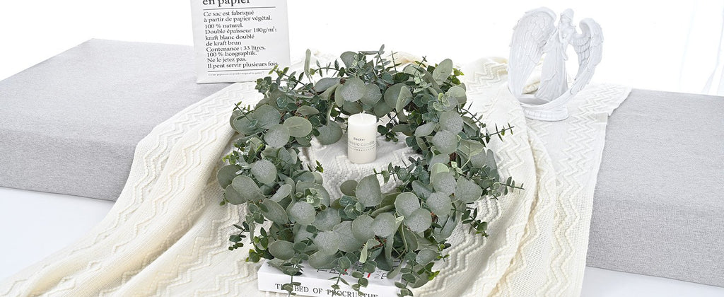 Artificial eucalyptus garland arranged in a circle on a book, with a candle and angel statue nearby.
