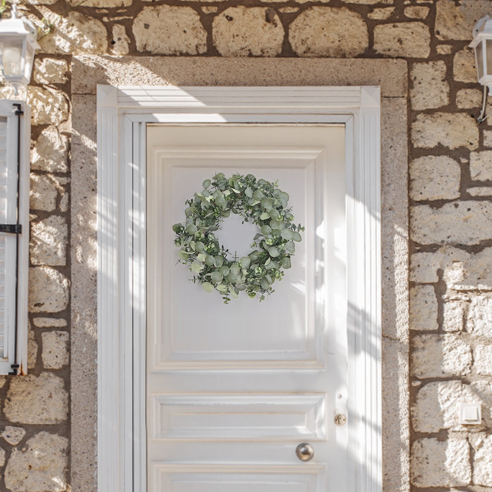 Artificial eucalyptus wreath hanging on a white wooden door with stone wall exterior