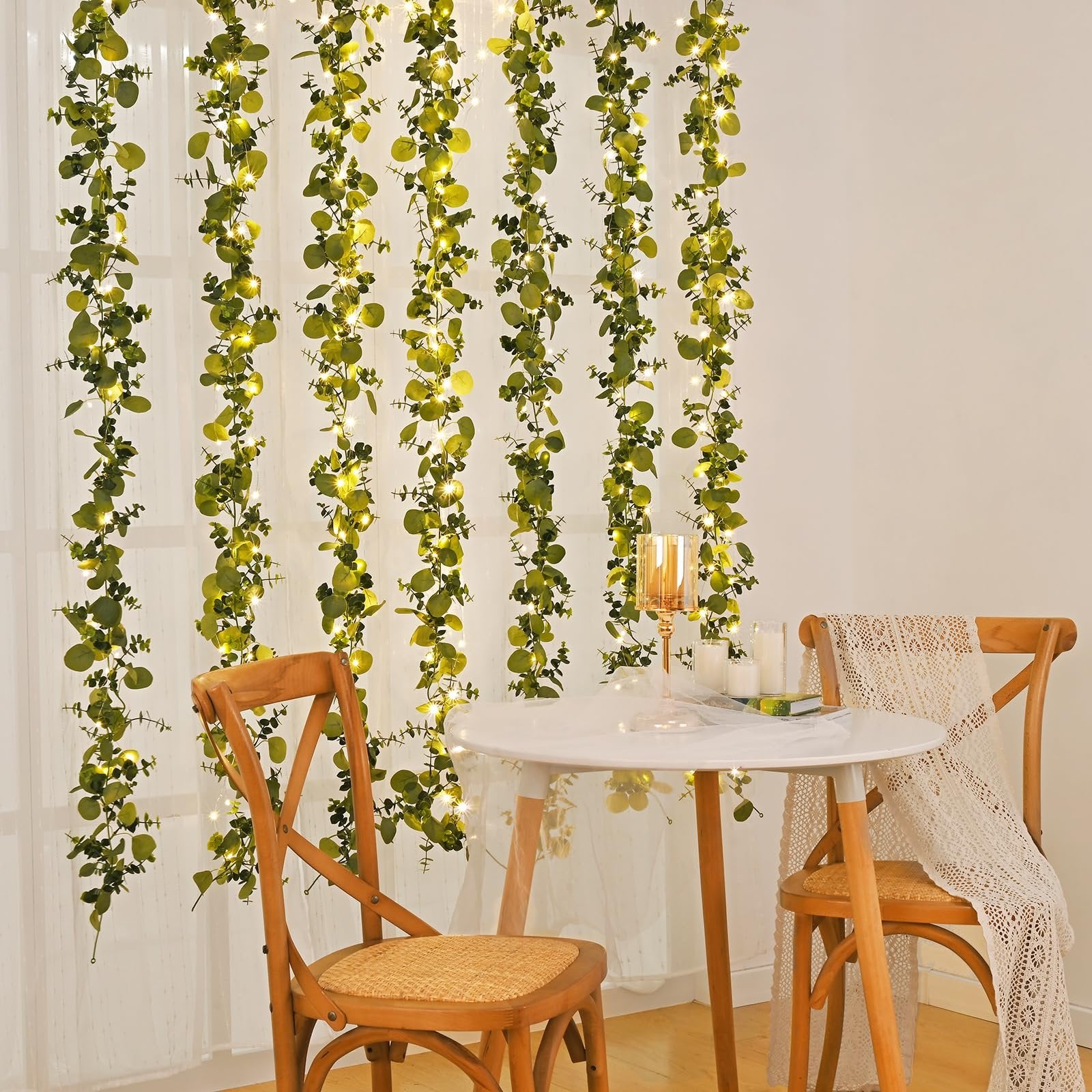 Artificial eucalyptus garland with fairy lights draped behind a table and chairs
