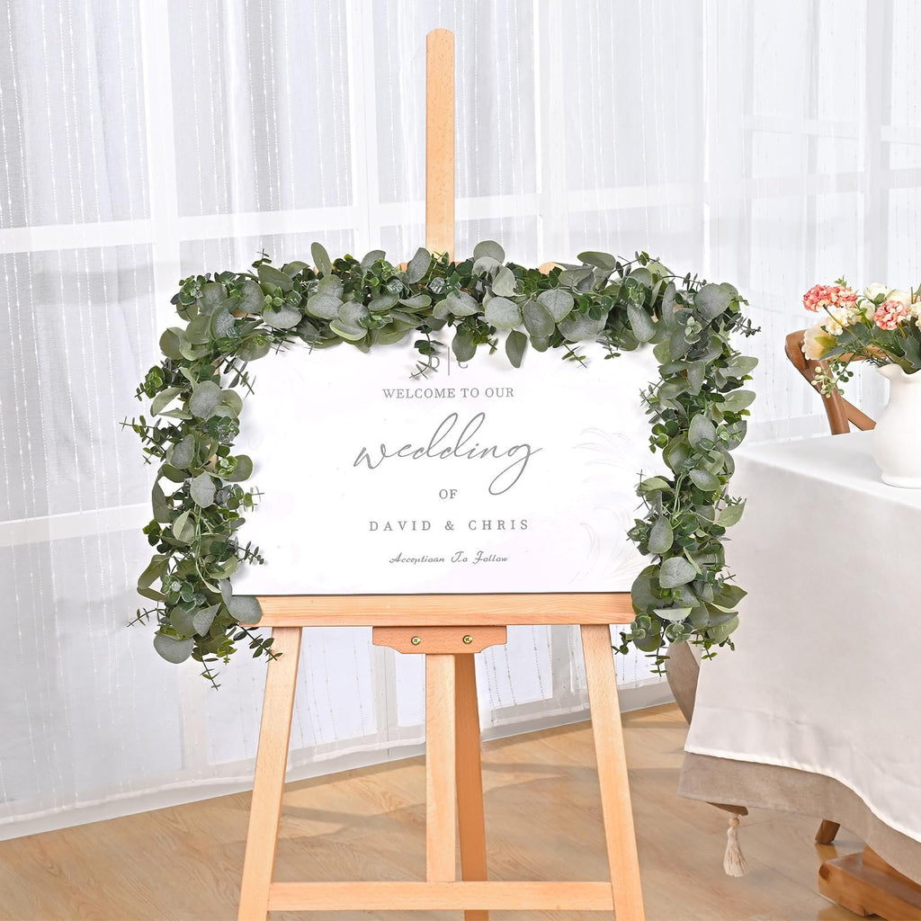Artificial eucalyptus garland draped around a wedding welcome sign on an easel.