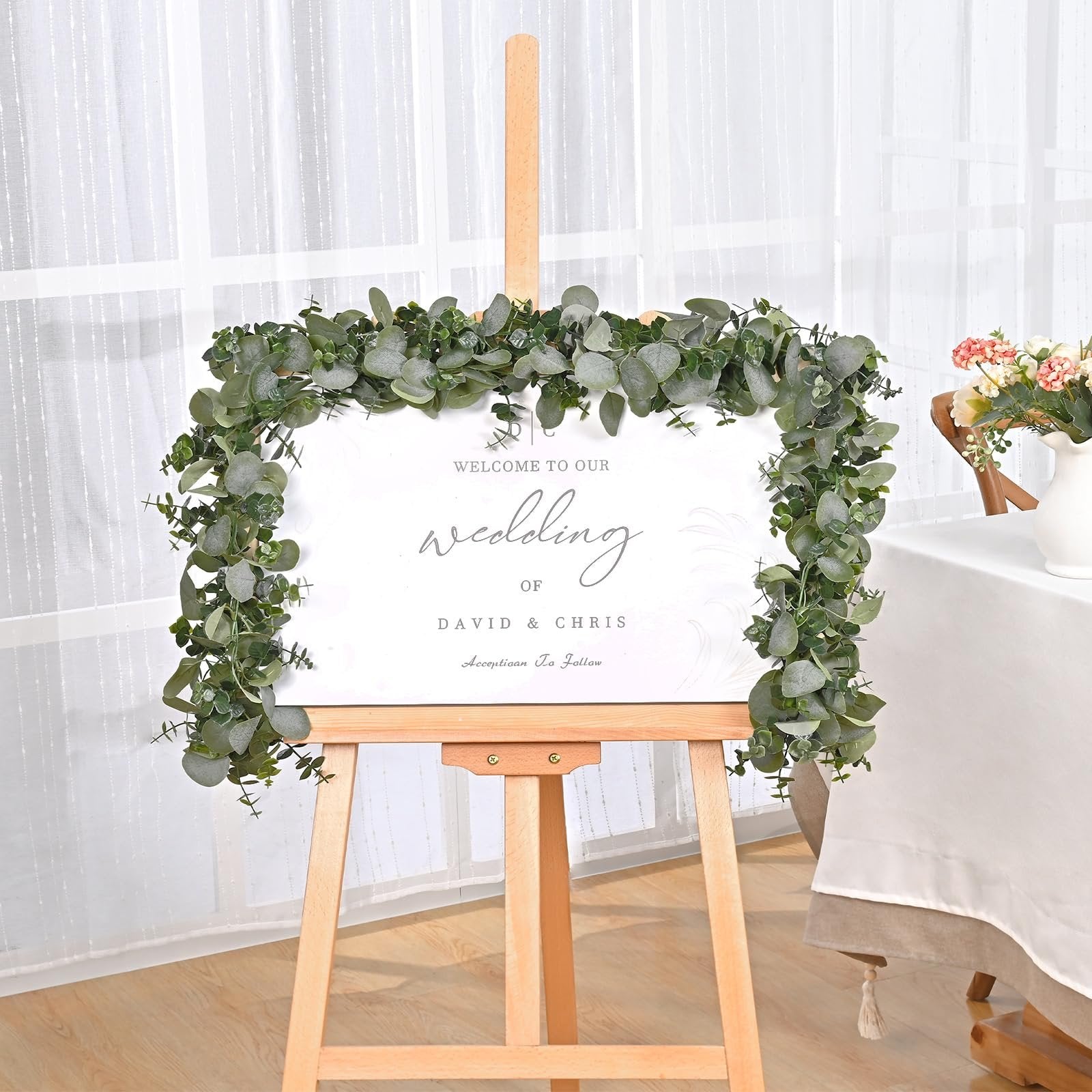 Artificial eucalyptus garland draped around a wedding welcome sign on an easel.