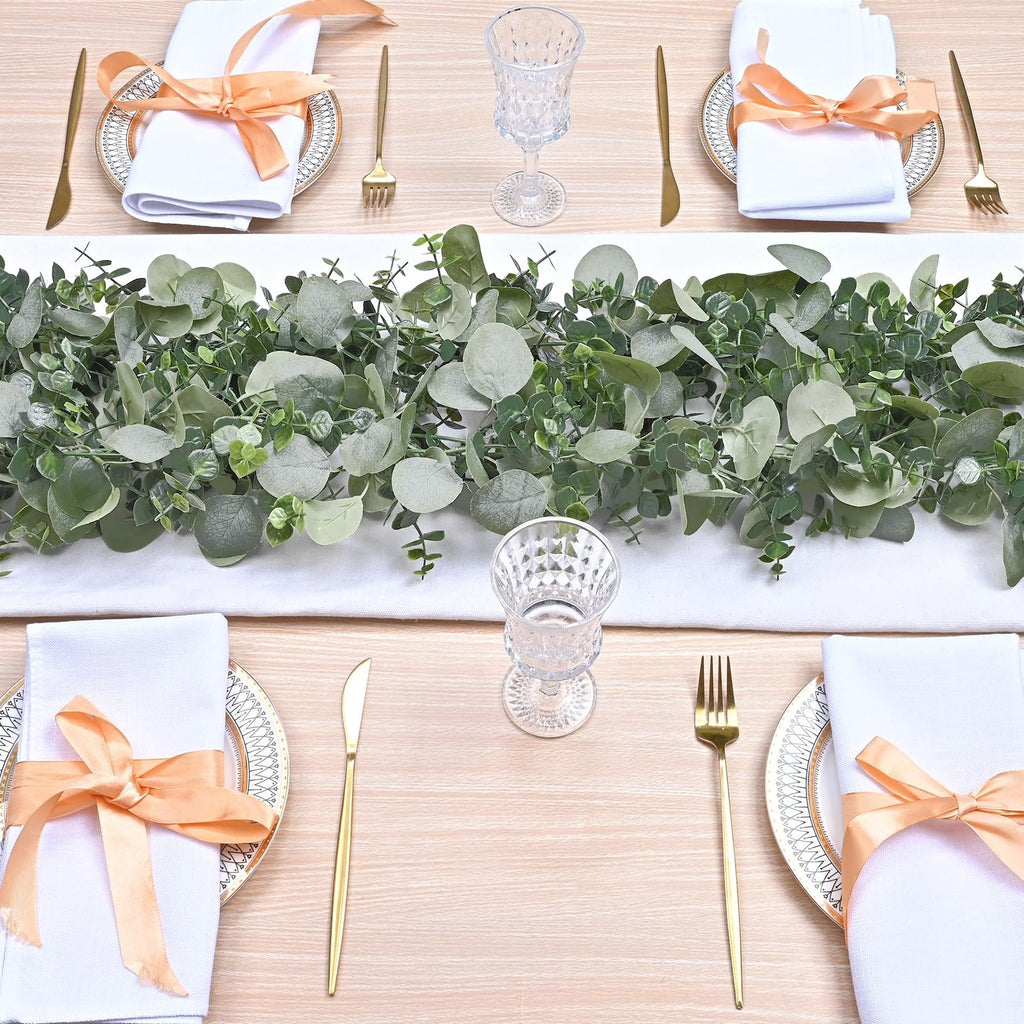 Table setting with artificial eucalyptus garland, white runner, and gold cutlery