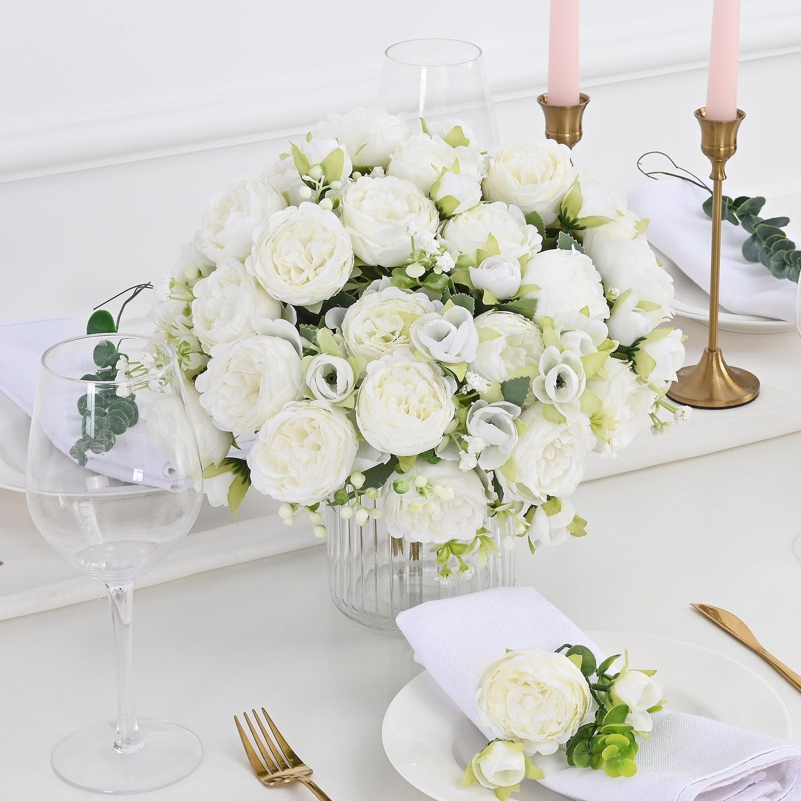 White artificial peony flower bouquet centerpiece on a table setting with gold cutlery and pink candles.