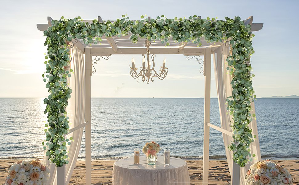 Artificial eucalyptus garland draped over a beach wedding arch with ocean backdrop and floral arrangements.