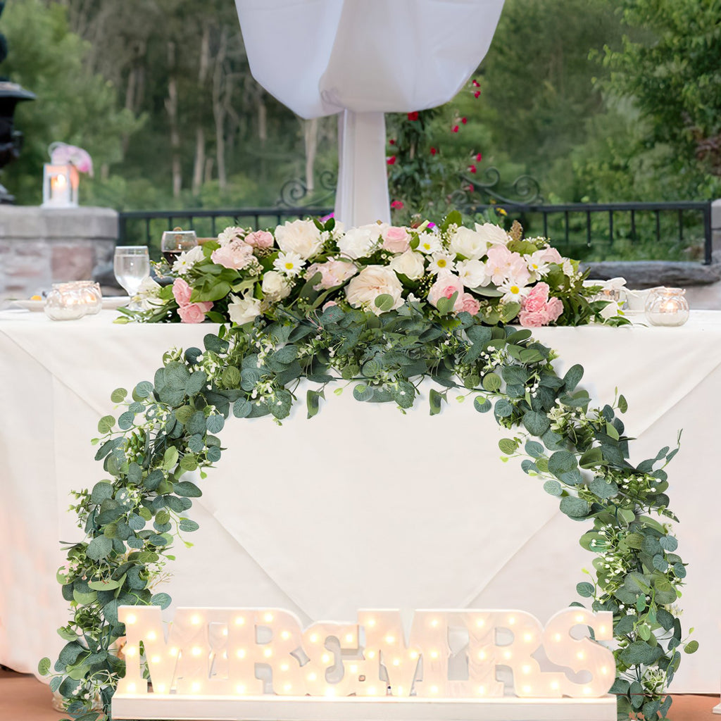 Artificial eucalyptus garland with white flowers draped over a table with illuminated MR & MRS letters