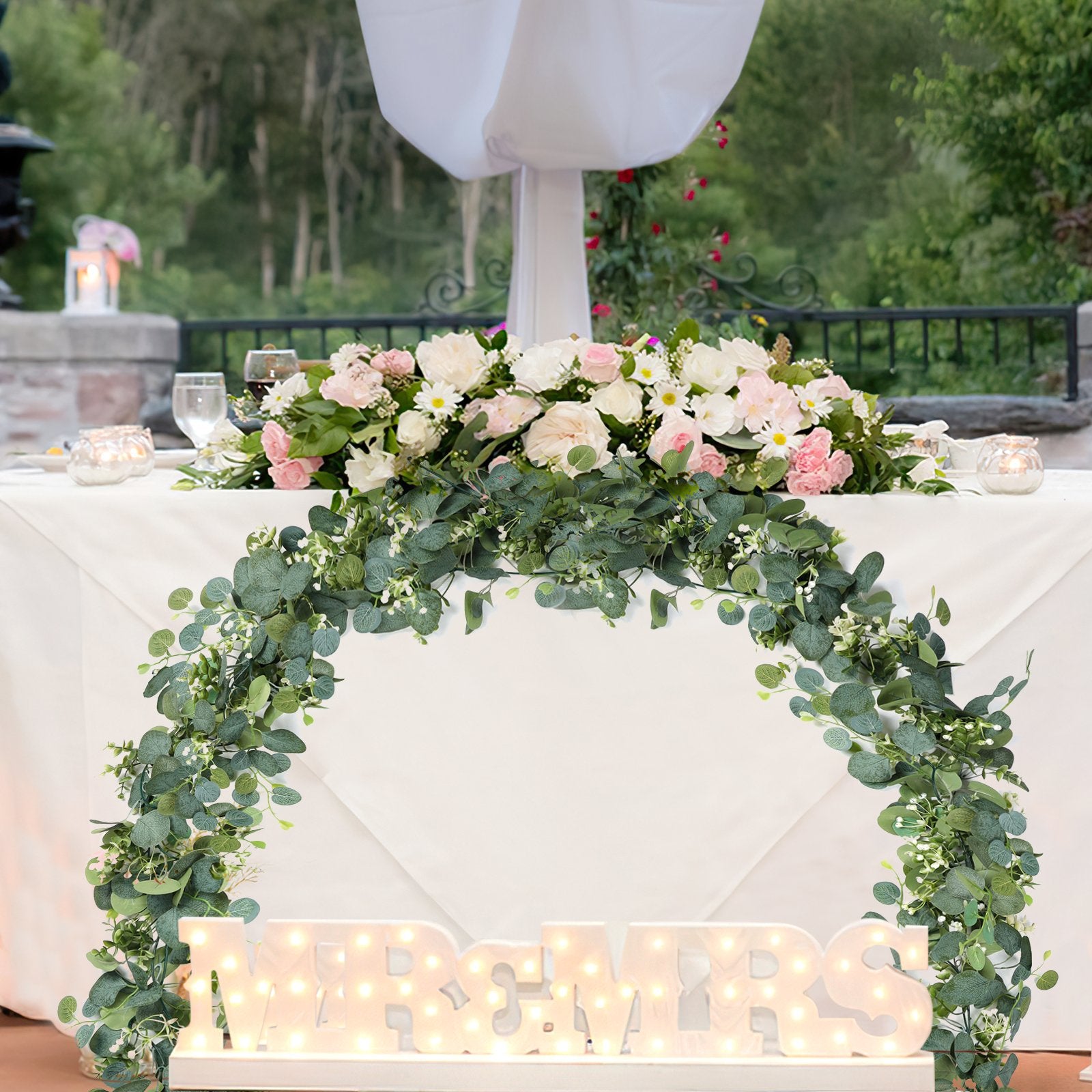 Artificial eucalyptus garland with white flowers draped over a table with illuminated MR & MRS letters