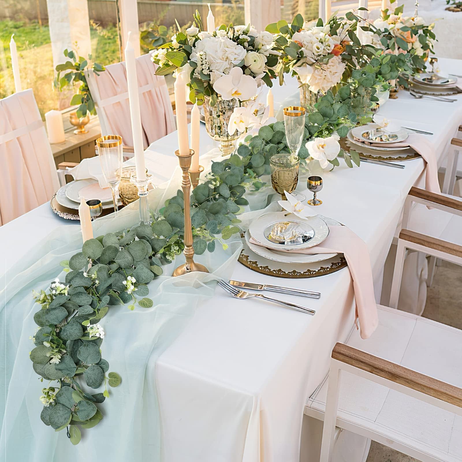Eucalyptus garland with white flowers draped across a formal table setting with candles and floral arrangements.