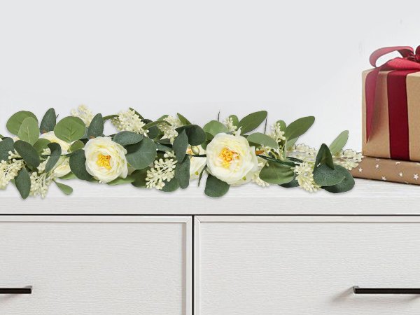 Artificial eucalyptus garland with white roses and gypsophila on a dresser with gift boxes