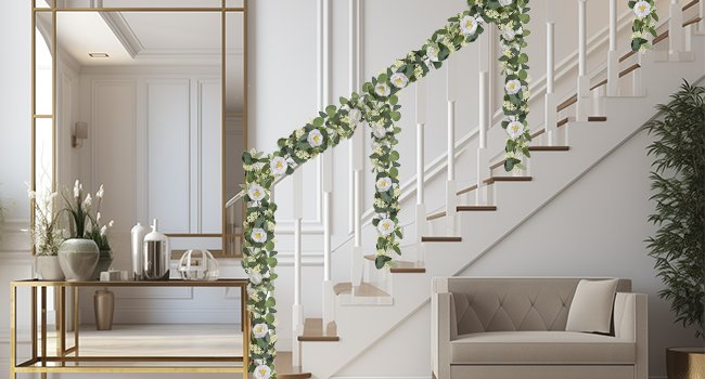 Artificial eucalyptus garland with white roses draped along a staircase railing and banister.