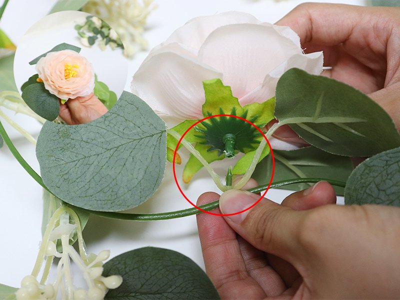 Close-up of artificial eucalyptus garland with pink roses and white gypsophila being assembled by hands.