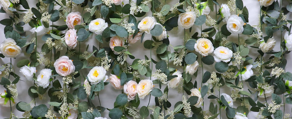 Artificial eucalyptus garland with pink and white roses and seeded leaves against a white background.
