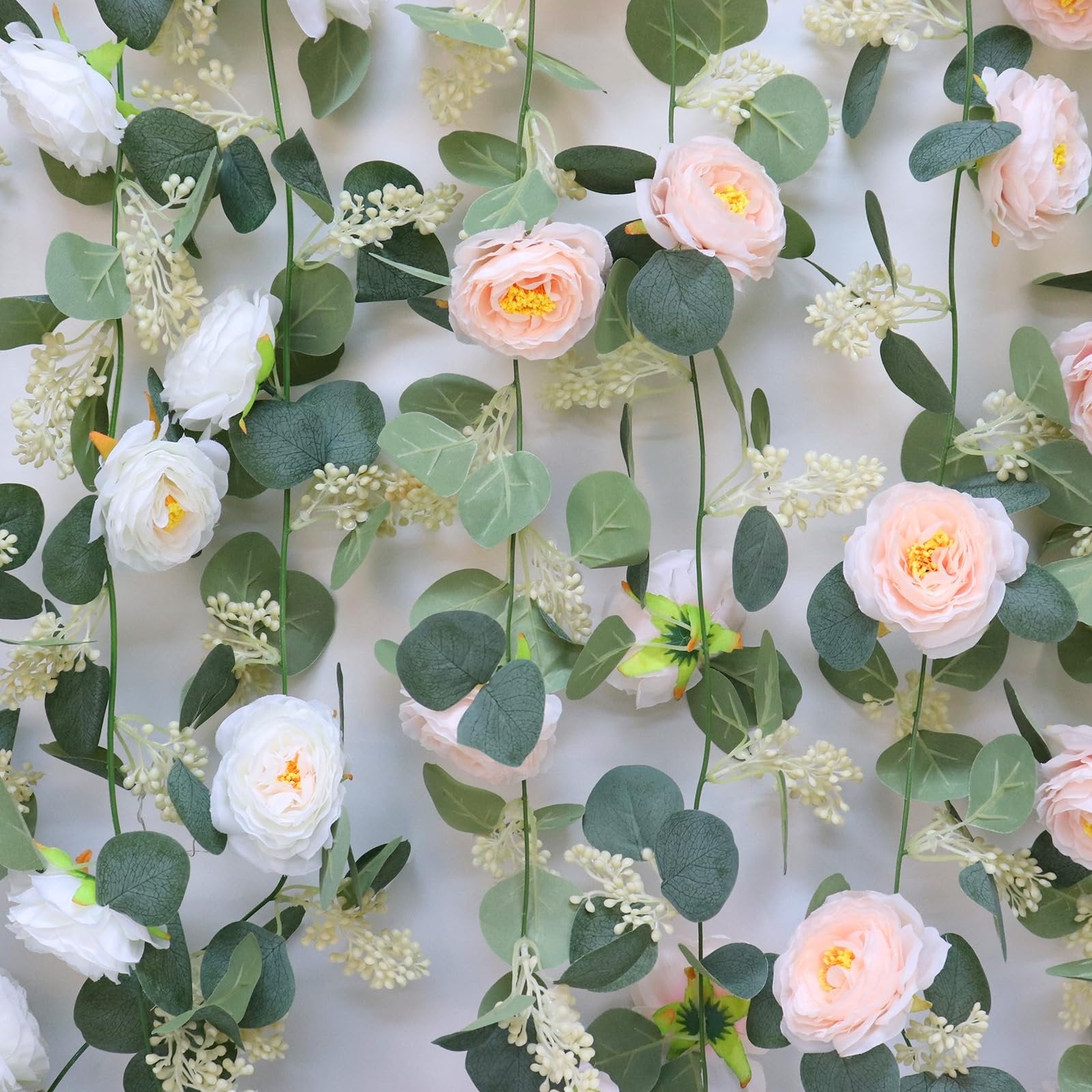 Artificial eucalyptus garland with pink and white roses and seeded leaves against a white background.