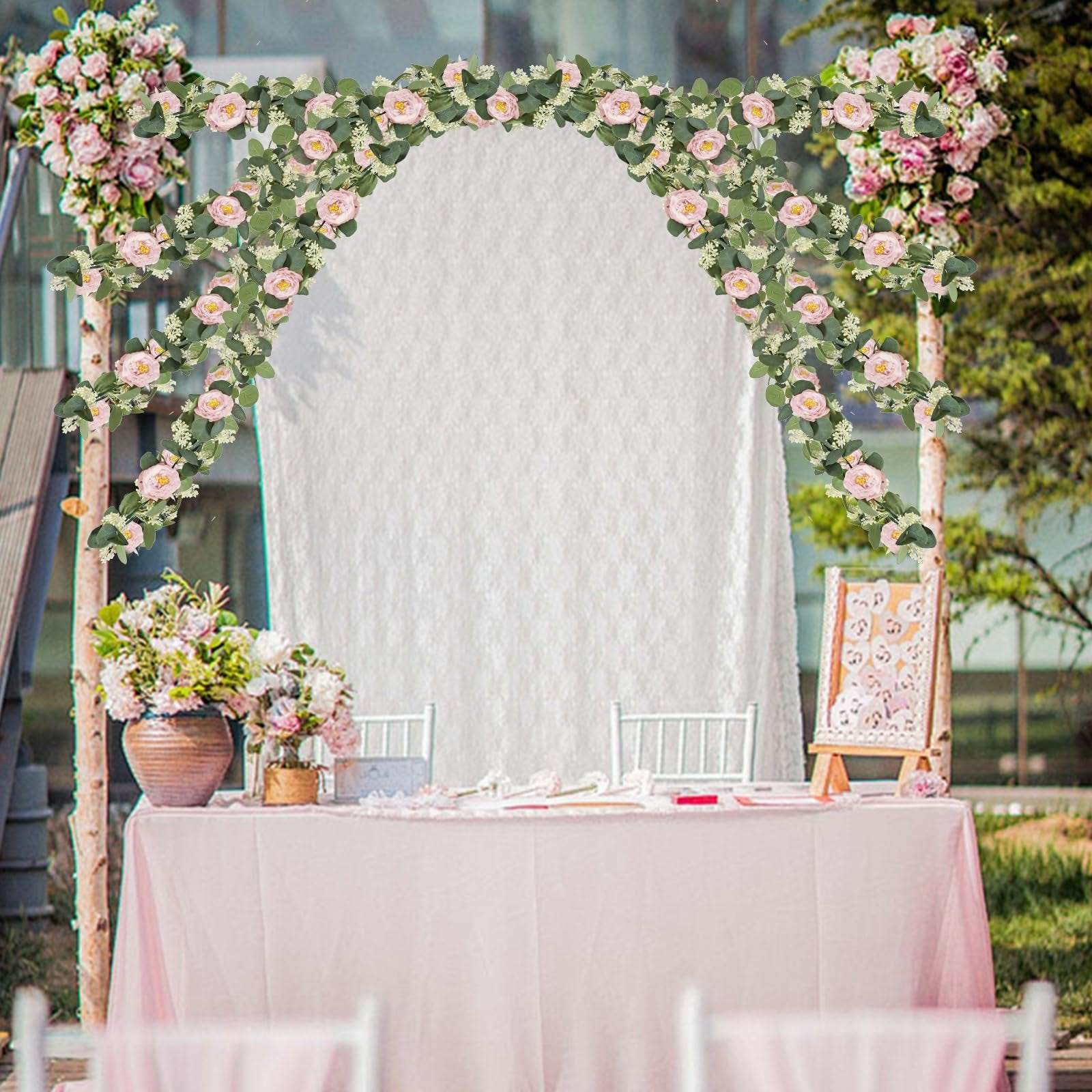 Artificial eucalyptus garland with pink roses and white gypsophila draped over a wedding arch and table