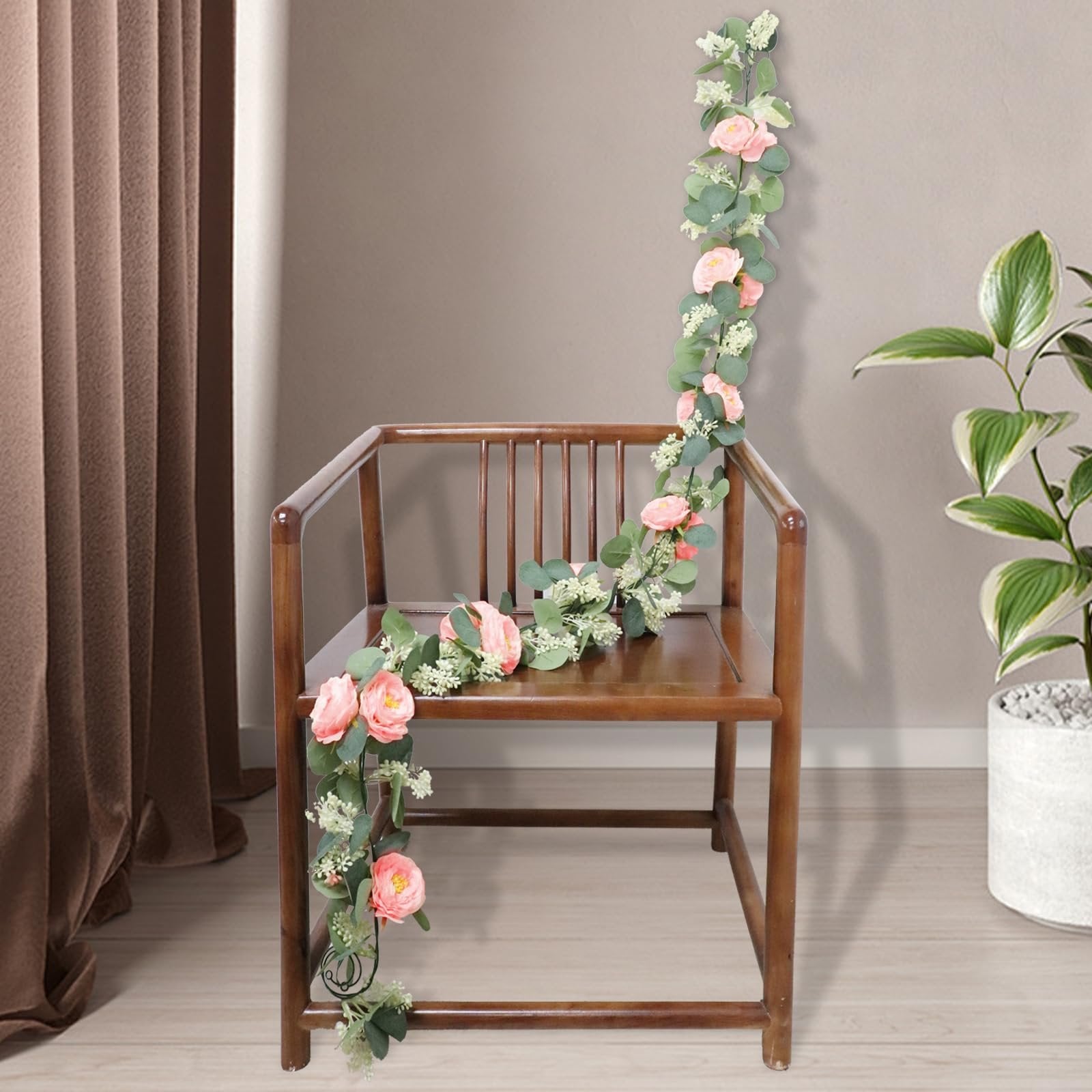Artificial eucalyptus garland with pink roses draped over a wooden chair