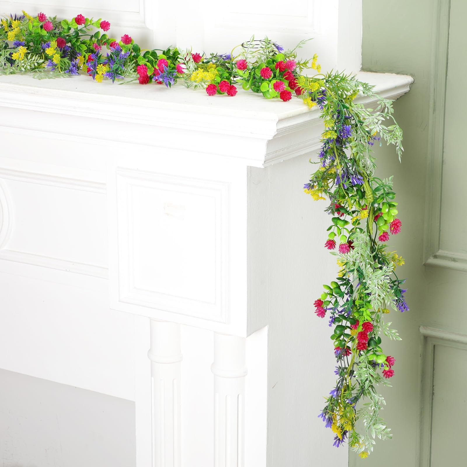 Artificial wildflower garland with pink, yellow, and purple flowers draped over a white mantlepiece.