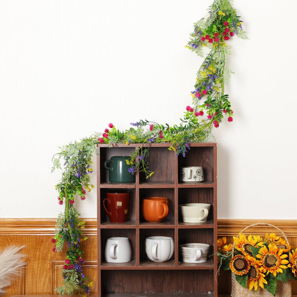 Artificial wildflower garland with daisies and lavender draped over a wooden shelf filled with mugs and a sunflower basket.