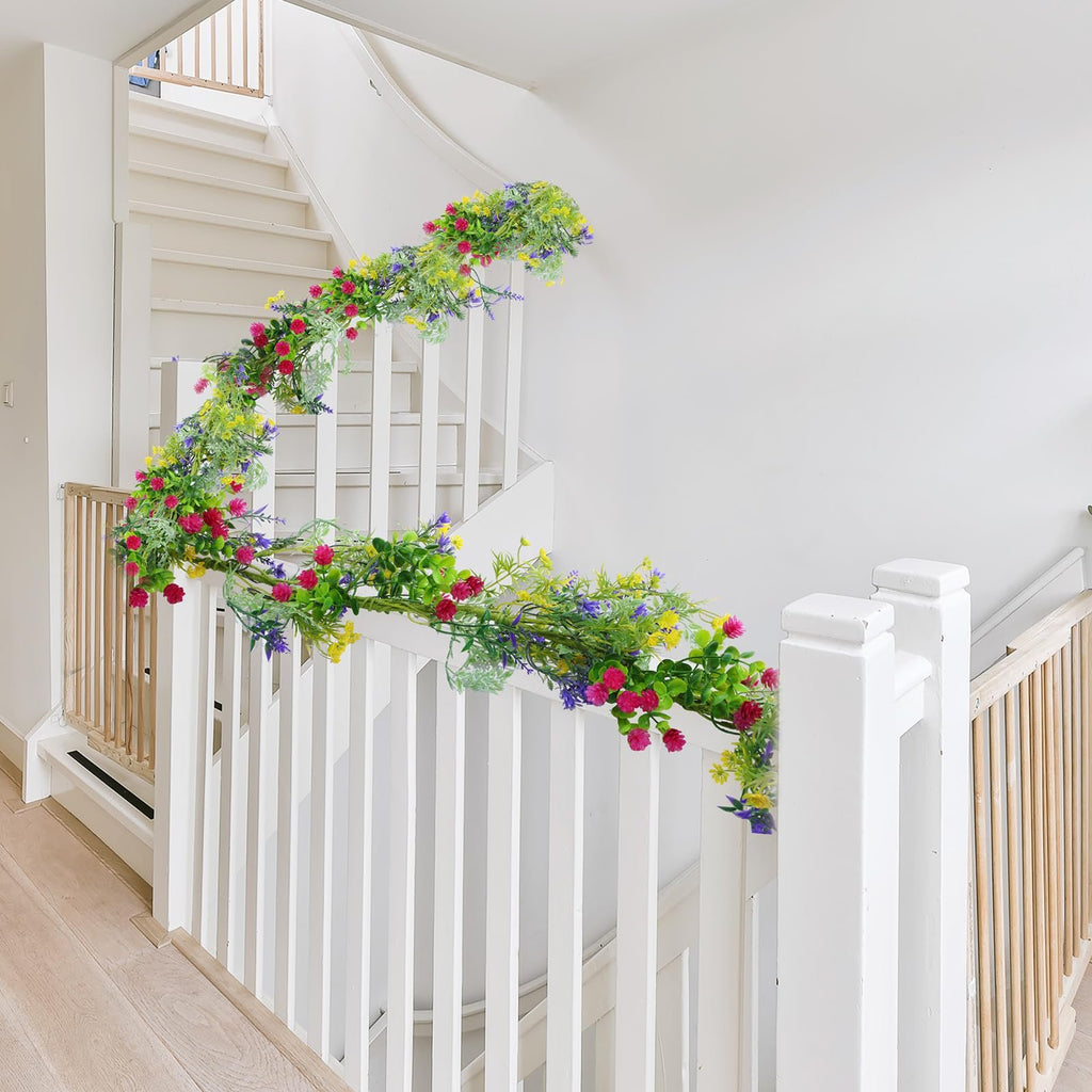 Artificial wildflower garland with pink, yellow, and purple flowers draped on a white staircase railing.