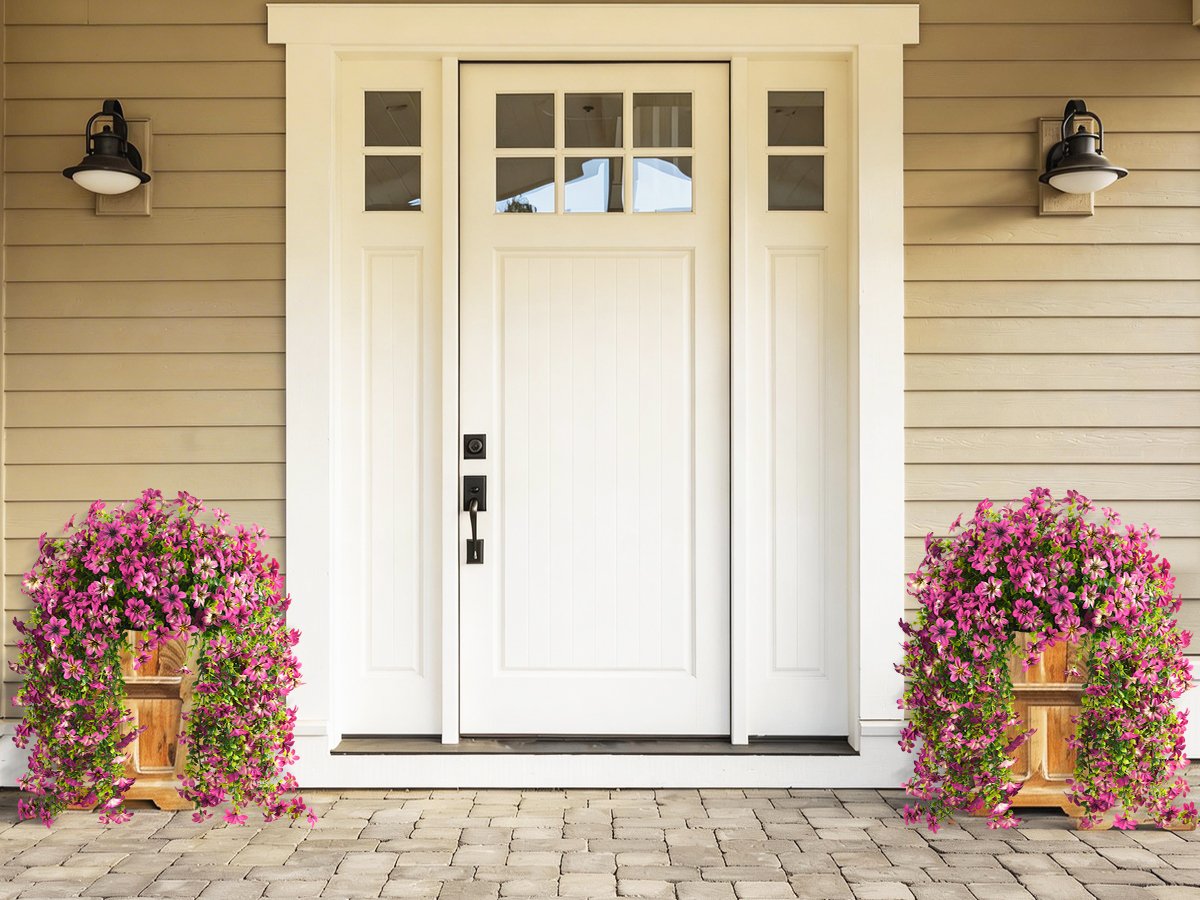 Two wooden planters filled with vibrant purple artificial flowers flanking a white front door.