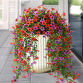 Artificial hanging flowers in red and purple cascading from a cream planter on a porch.