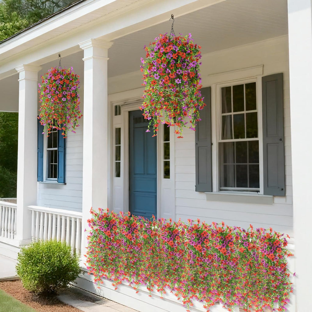 Two hanging baskets of red and purple artificial flowers adorn a white porch with blue shutters and a blue door.