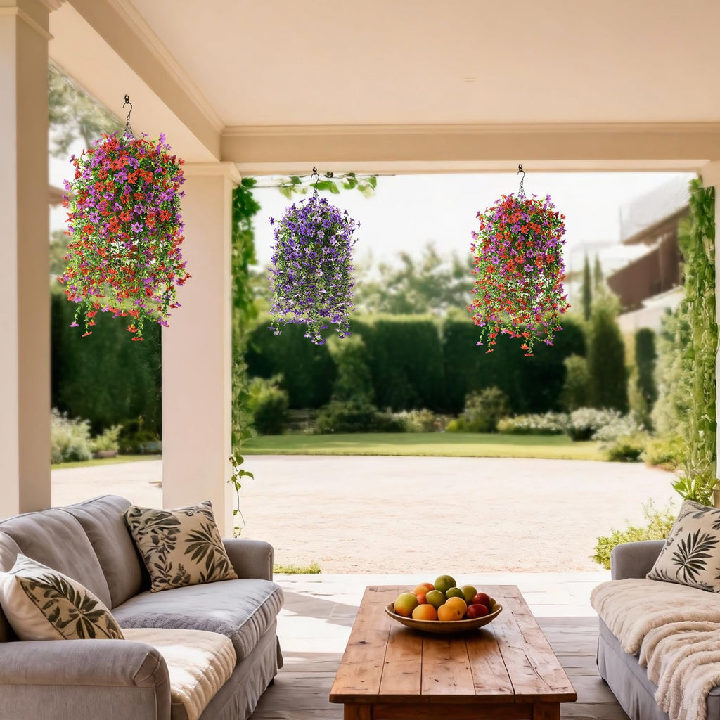 Three hanging baskets of artificial flowers, red/purple and purple, displayed on a covered porch with sofas and a coffee table.