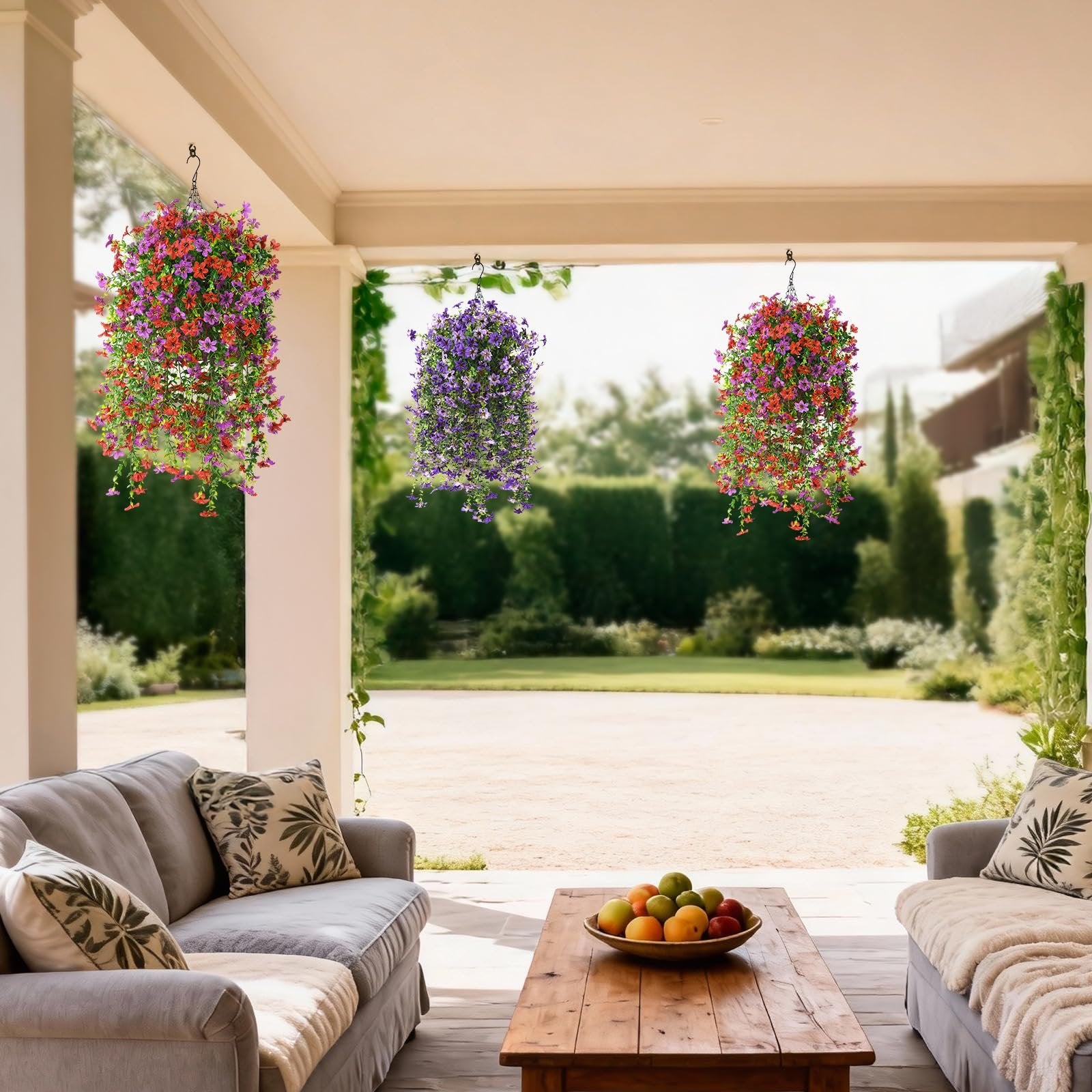 Three hanging baskets of artificial flowers, red/purple and purple, displayed on a covered porch with sofas and a coffee table.