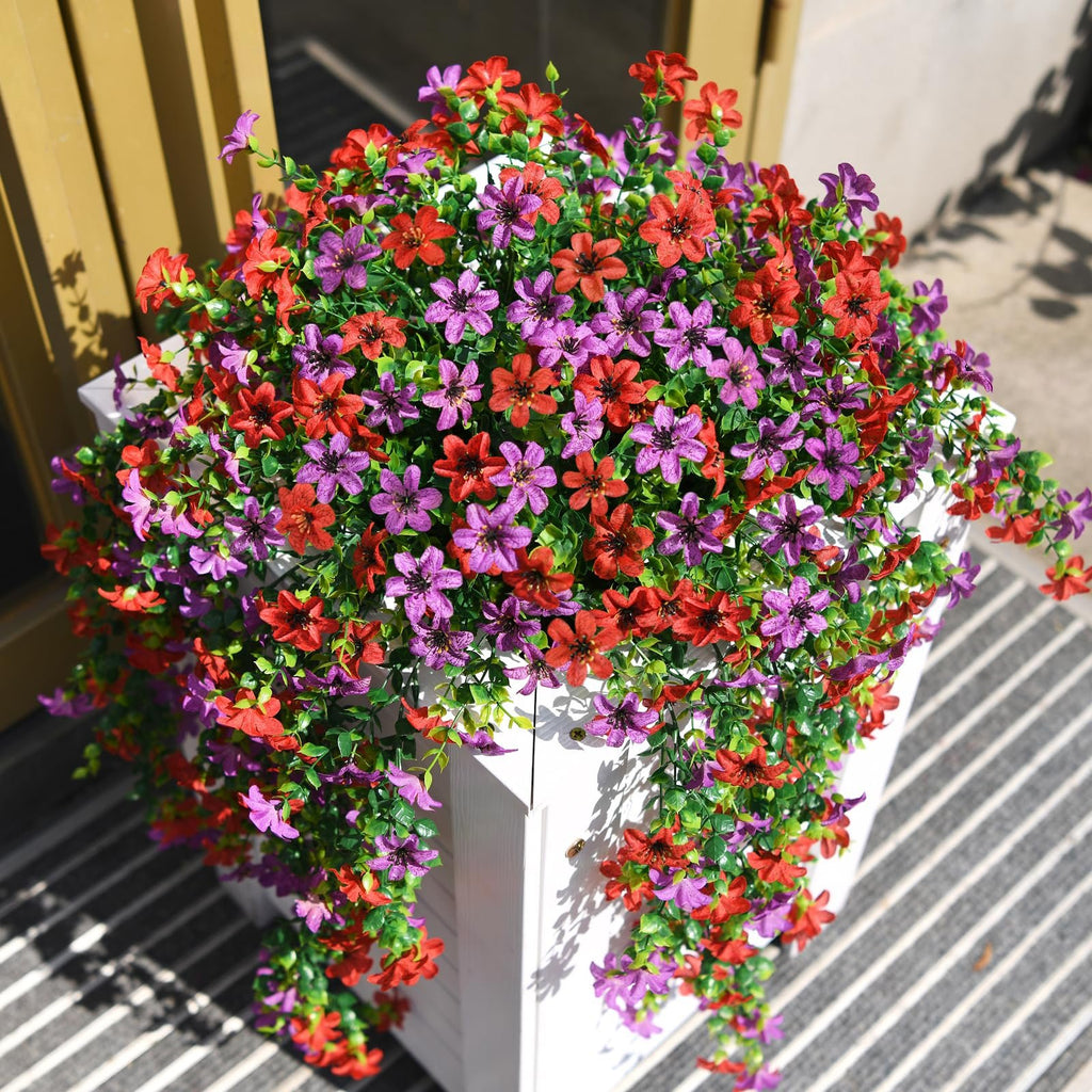Artificial hanging flowers in red and purple cascade from a white planter on a striped mat.