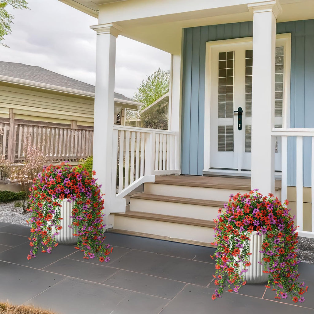 Two white planters filled with red and purple artificial hanging flowers on a porch next to stairs.