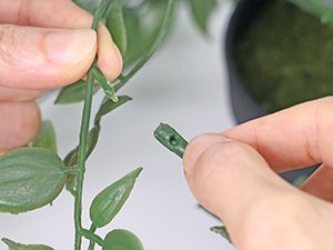 Close-up of hands assembling an artificial mandala vine plant, showing a stem piece being attached.