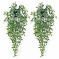 Two artificial green hanging plants with black pots against a white background