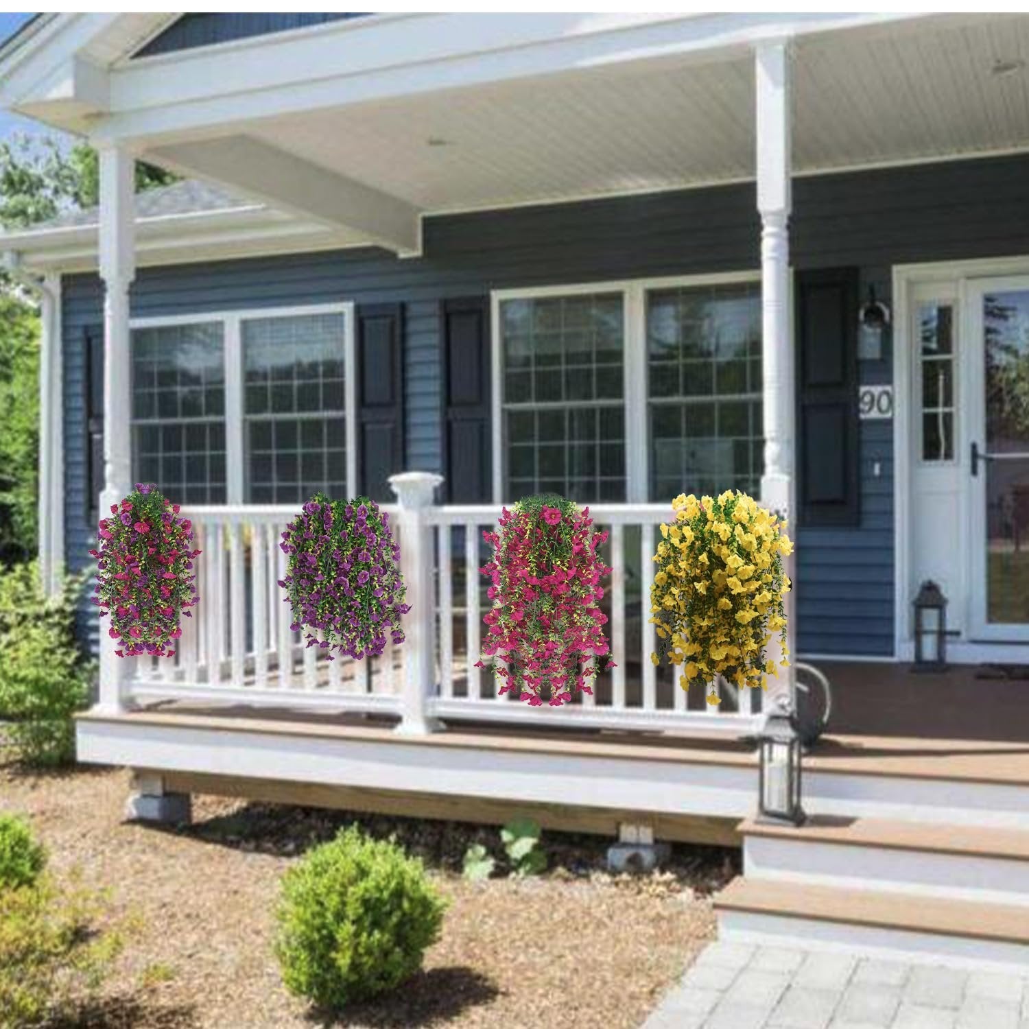 Four hanging baskets of artificial flowers in purple, pink, and yellow colors decorating a porch railing.