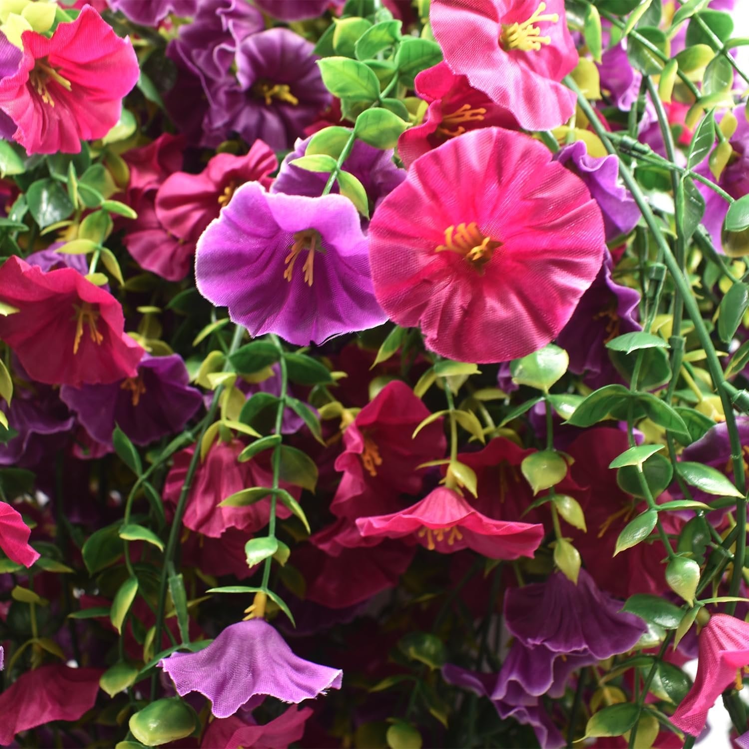 Close-up of artificial morning glory flowers in shades of purple and fuchsia with green leaves.