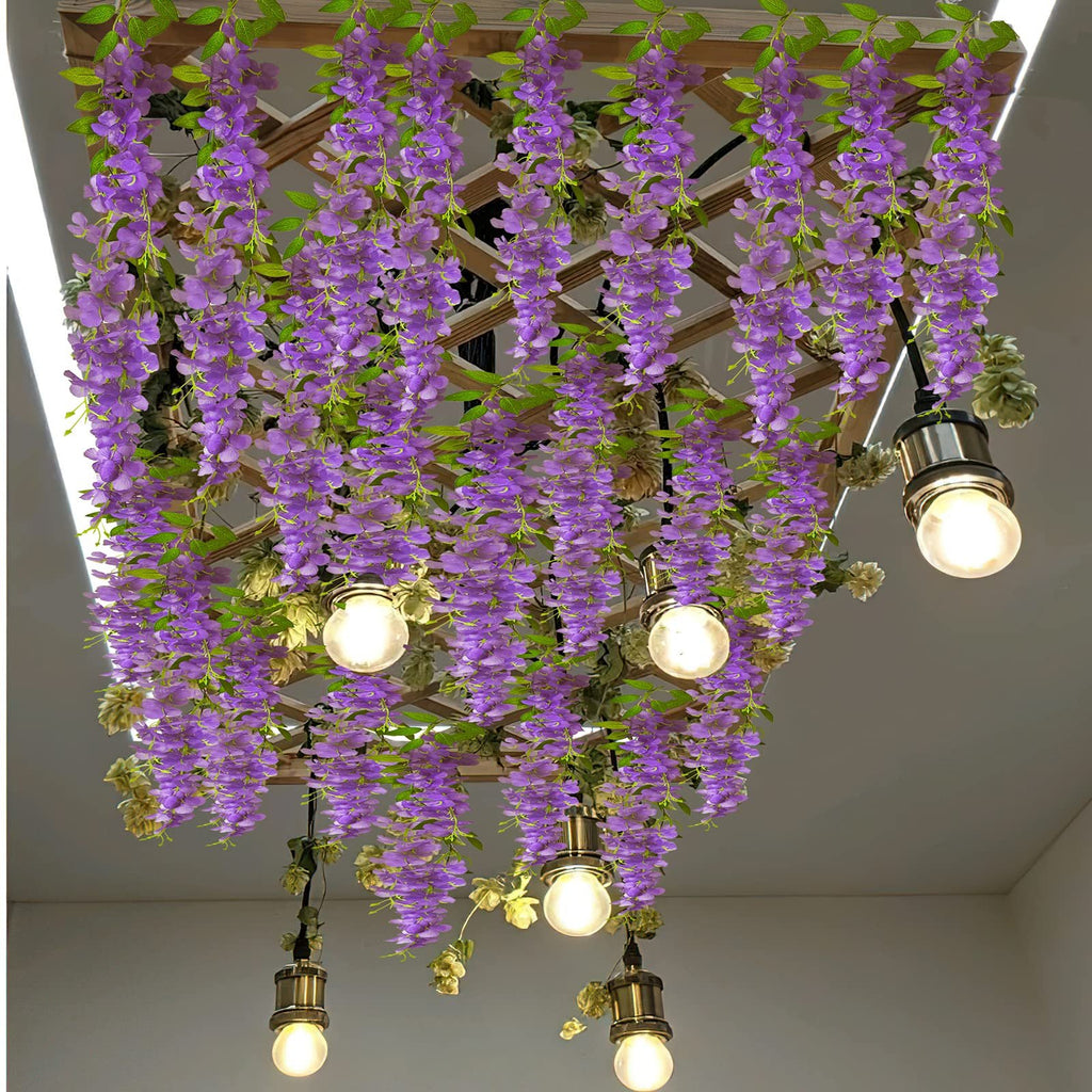 Artificial purple wisteria vines with green leaves hanging from a wooden lattice, with pendant lights.