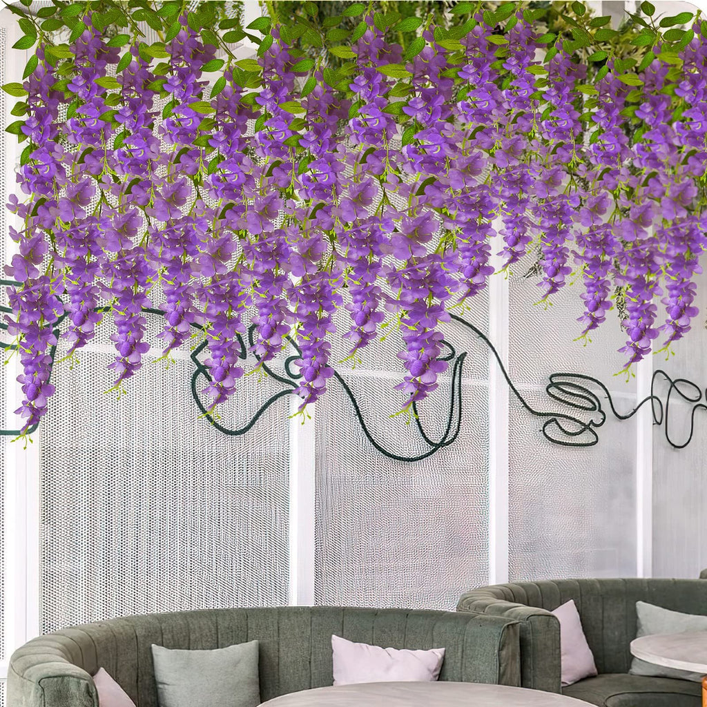 Artificial purple wisteria hanging vines with green leaves draped over a white textured wall with dark green wire art.