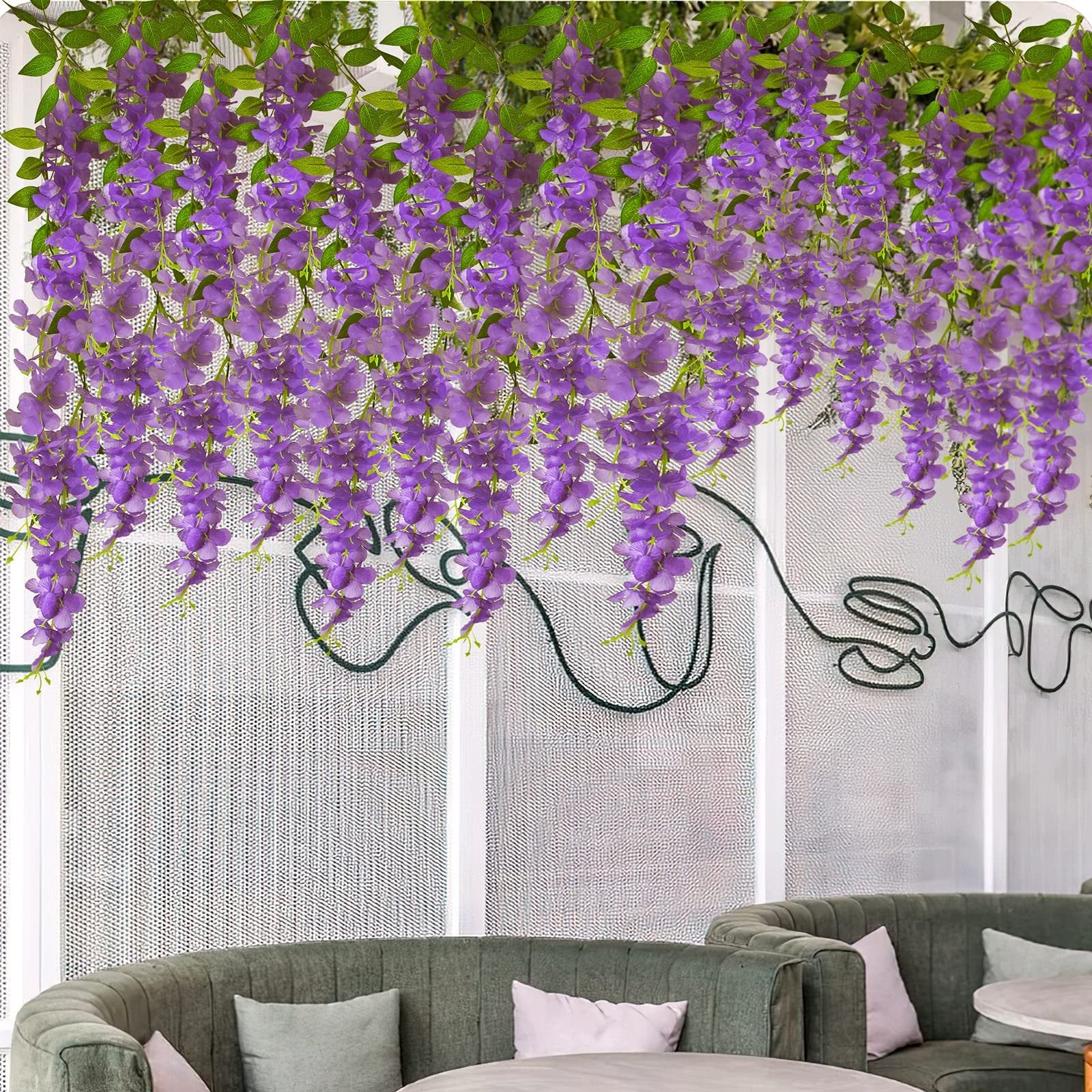 Artificial purple wisteria hanging vines with green leaves draped over a white textured wall with dark green wire art.